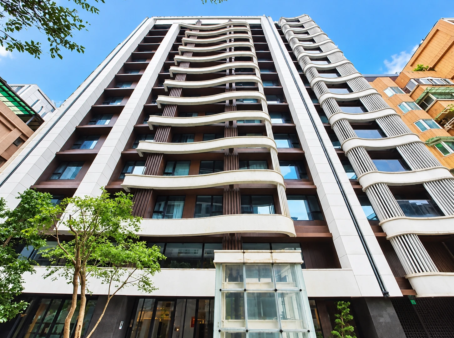 御中央Ⅱ建築外觀，仰角望向弧形陽台立面與街邊植栽